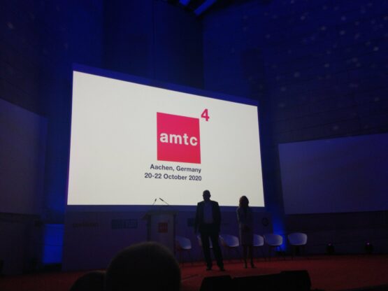two business people on stage with a screen on background with the logo of amtc4